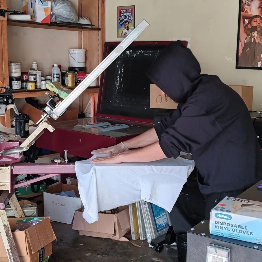 Person in a black hooded outfit cleaning a sword indoors.