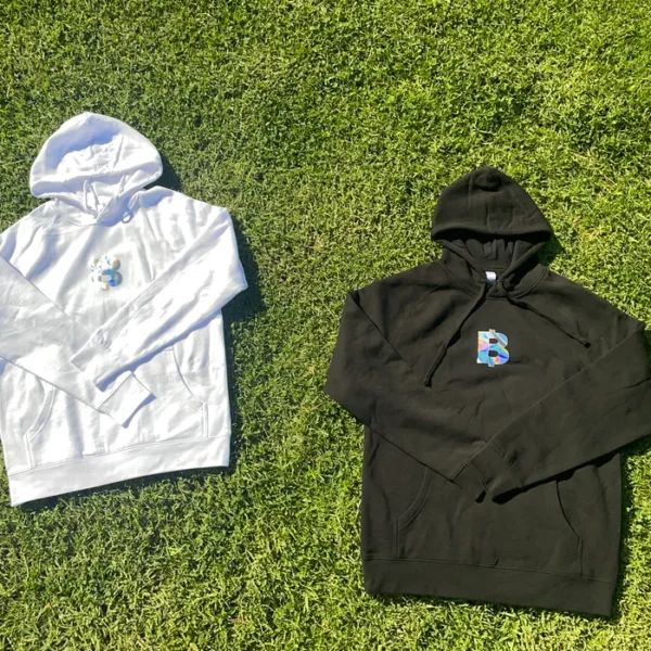 Two hoodies, one white and one black, laid on grass.