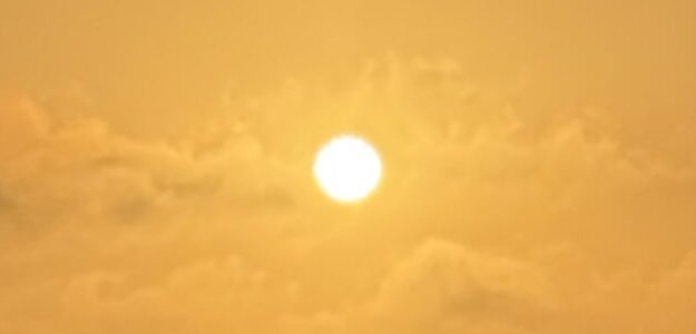 Bright sun shining in a golden sky with soft clouds.