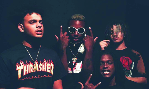 Three young men posing with hand signs in a dimly lit setting.