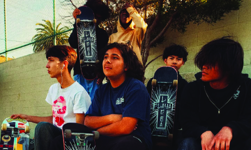 A group of young people sitting with skateboards outdoors.
