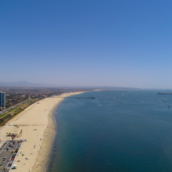 Aerial view of a long sandy beach meeting a calm blue ocean under a clear sky.