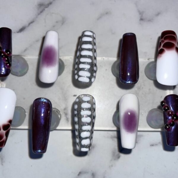 Set of purple and white press-on nails with various designs.