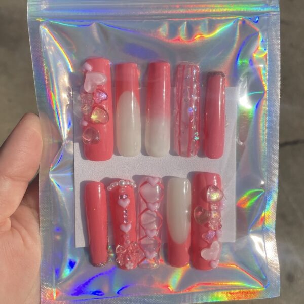 Set of pink and red decorated press-on nails in holographic packaging.